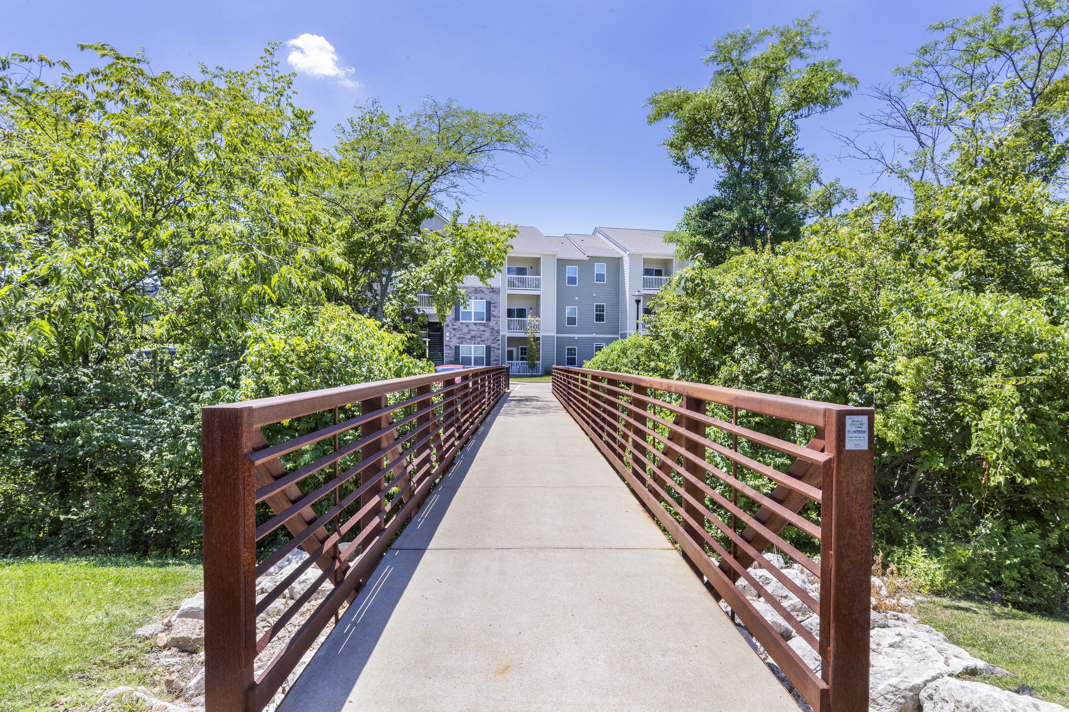 a bridge with a building in the background and trees at Aventura at Towne Centre, Missouri, 63011